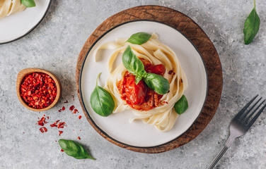 Pasta Tagliatelle Bolognese with meat tomato sauce and fresh basil leaves on white plate. Light gray table. Top view