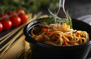 Italian cuisine. Bolognese pasta in a black plastic bowl with a fork and dill. Dry pasta, tomatoes and a bunch of dill. Macaroni with meat and vegetables. Closeup. Background image, copy space
