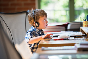 A schoolboy boy studies at home and does school homework listening to lesson with headphones....