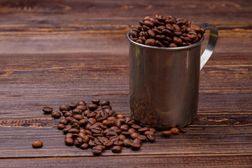 Silver coffee pot filled with coffee beans. Brown wooden table surface.