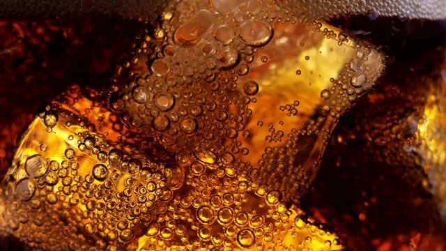 Close-up of filling a carbonated soft drink in a transparent glass with ice cubes. Foam and air bubbles with ice in a glass of soda. Cocktail with whiskey and rum. Ice drink. Drinking carbonated soda.