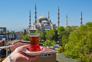 Naklejka premium Woman's hand holding cup with Traditional turkish tea in front of Blue mosque aka Sultanahmet Camii in Istanbul, Turkey.