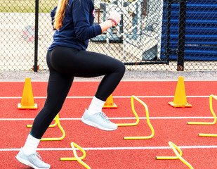 Female stepping over yellow mini hurdles at practice on a track