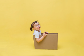 A cute girl sits in a cardboard box and looks at the camera. A little girl smiles in a white...