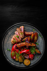 fried meat with potatoes, pepper, tomatoes, herbs and spices in plate on black wooden table background