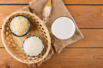 Rice milk and rice seeds on wooden boards. Rice milk in glass on sackcloth. Vegan non-dairy milk on wooden background. Alternative milk from rise. Rustic style. Top view