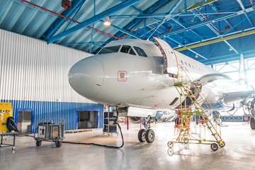 Airplanes under repair in a maintenance hangar. View of the nose and cockpit, open front door with...