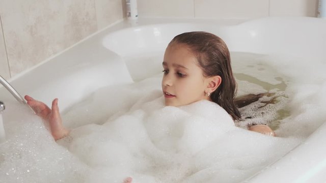 Close-up of a pretty little girl bathing full of foam in the bathroom. Hygiene and Baby Care Concept, HD still video camera, 4x slow motion.