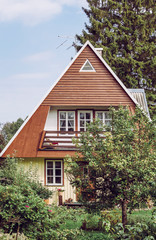 Cute retro small country house with lush green garden on sunny summer day. Windows with grids and yellow painted wooden board walls.
