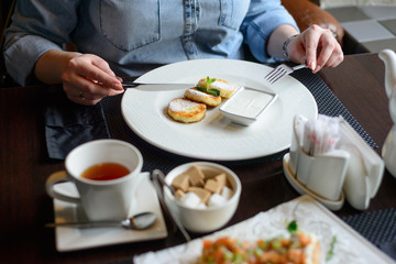 morning Breakfast or brunch in the restaurant. table with drinks and food. women's hands cut cheesecakes with a knife and fork. selective focus