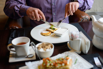Obraz na płótnie Canvas morning Breakfast or brunch in the restaurant. table with drinks and food. man hands cut cheesecakes with a knife and fork. selective focus