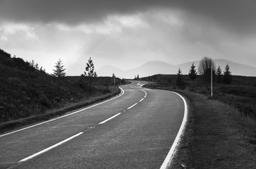 A monochrome image of a winding road cutting through the scenic Scottish Highlands.