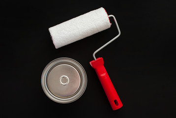 Red white paint roller and a can of paint on a black background. View from above