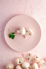 Fototapeta na wymiar Champignon mushrooms healthy food on pink plate with parsley greenery on pink textured background, top view