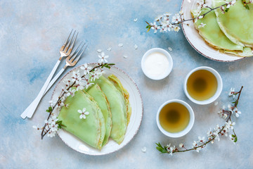 Delicious homemade green pancakes with blossoming cherry tree branches with green  tea on sky blue background. Top view, close up