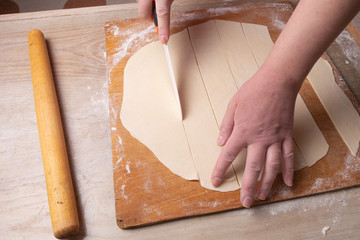 Female hands slices the dough on a cutting board with a white knife. Cooking at home.