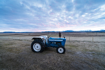 Agriculture stock picture. A small tractor on a field during the sunset time. Agriculture in Iceland, Scandinavia. Background photograph of a tractor