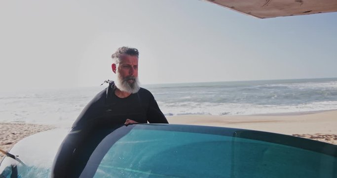 Senior handsome man removing surfboard from van at the beach