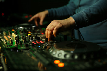 dj's hand is mixing tracks at party in night club. disc jockey playing music on the modern...