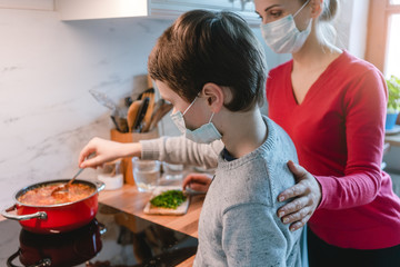 Mother and son cooking at home together wearing masks