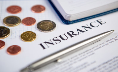 Closeup the silver modern pen on insurance contract with coins and planning in background.