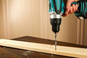 carpenter's hand is drilling wood plank by cordless drill close up with copy space