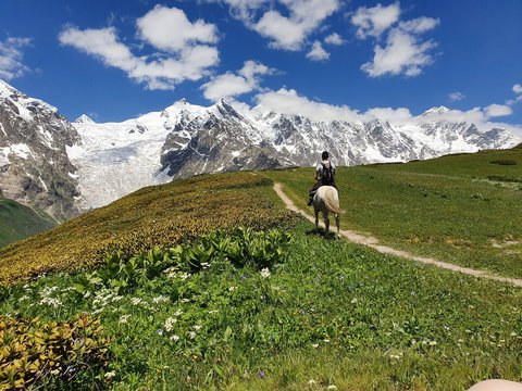 Man riding horse at the top of a pass in Svaneti region, Georgia.  Adishi Glacier of the Caucas mountain in behind. Beautiful summer day at the top of mountain.