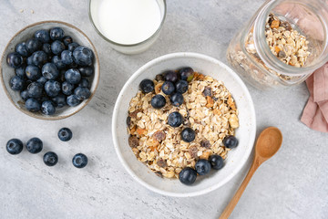Obraz na płótnie Canvas Granola or muesli in bowl with blueberries. Healthy breakfast cereals, oat granola with fresh blueberries and glass of milk on grey concrete background. Concept of clean eating, healthy lifestyle