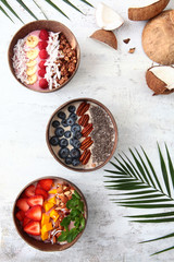 Balinese-style breakfasts. Muesli with yogurt and berries in plates made of coconut skin. Tropical tree leaves and coconuts. Light textured background. Wholesome breakfast.