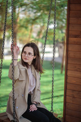 Stylish girl with glasses looks away, outdoors. Teenager girl on a swing, beautiful portrait.