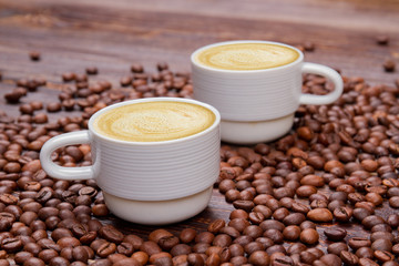 Two cups of coffee beans with milky foam. Close up pile of roasted coffee beans.