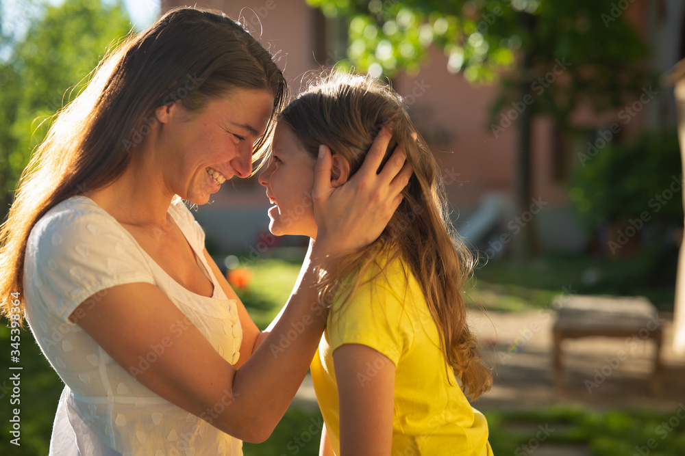 Wall mural Authentic shot of happy little daughter and young mother are enjoying their time together outside their house on a sunny day. Concept: family, motherhood,life, happiness, childhood, authenticity