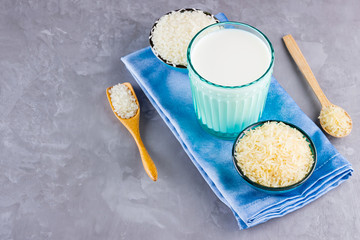 Rice milk and rice seeds on a gray background. Rice milk in glass on a blue napkin. Vegan non-dairy milk on cement background. Alternative milk from rise. Minimalism. Copy space