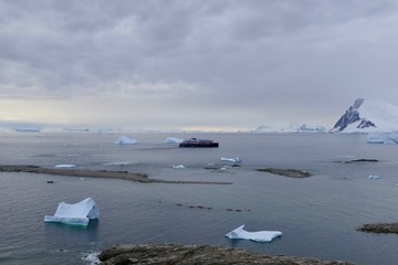 Antarctic island with cruise ship and bay with icebergs, stormy sky, Antarctica