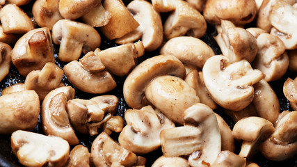 Sliced toasted champignon close-up. Mushrooms are fried in oil in a pan background
