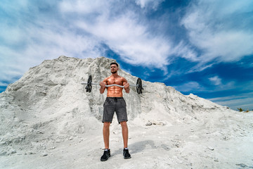 Muscular and bearded man doing exercises with barbell outdoors. Bodybuilding and outdoor sports concept. Photoshoot in a quarry.
