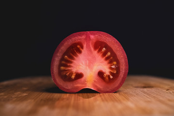 half a tomato lies on a cutting Board on a dark background. Ripe vegetables. Tomato set. Dark background. Healthy diet. Vegetarian food. Healthy diet. The design concept of the product.