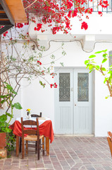 A cozy table outside of a restaurant in Crete. The table is under a balcony, climbing plants grow up the wall. Mediterranean flair.