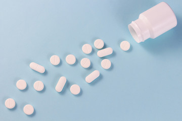 many pills on a blue background. White pills drop out of a white jar on a blue background.copyspace for text