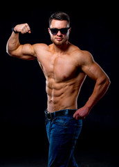 Fototapeta premium Strong brutal bodybuilder man with perfect abs, shoulders,biceps, triceps and chest showing his biceps. Blue filter on dark background