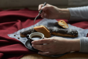 Woman eating eclairs filled with cream, traditional french eclairs with chocolate and cup of espresso, selective focus.