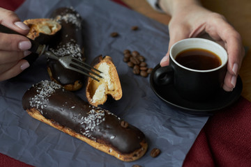 Woman eating eclairs filled with cream, traditional french eclairs with chocolate and cup of espresso, selective focus.