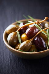 Various olives and capers on black stone background. Close up. 
