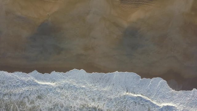 Flying over a sandy beach. Waves break on a sandy beach on the Atlantic coast, aerial View. Nazare, Portugal. (raw video).