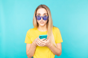 Young woman in dark glasses standing over blue isolated background looking at the camera. Youth and technology.