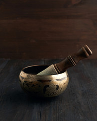 Tibetan singing copper bowl with a wooden clapper on a brown wooden table, objects for meditation