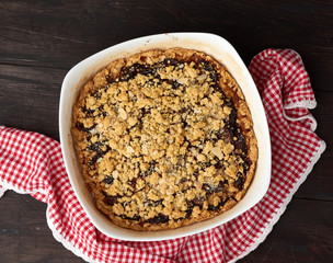 baked crumble pie with blue plum in a white ceramic plate on a wooden table