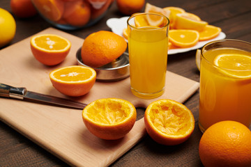 Fresh orange fruit whole and sliced on a wooden table, cutting board and kitchen knife. A plate full of citrus slices - natural and healthy food. Glass of fruit cocktail.