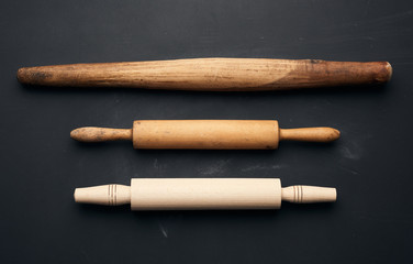 three types of wooden rolling pins for rolling dough on a black background