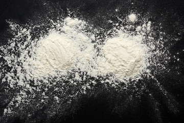 white wheat flour scattered on a black table, ingredient for the dough